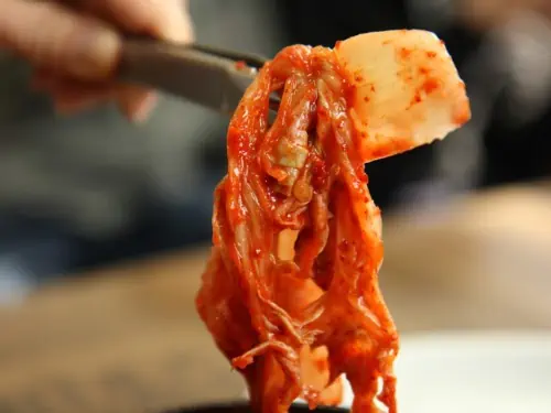 Some spicy, red coloured Korean Kimchi being held up with tongs