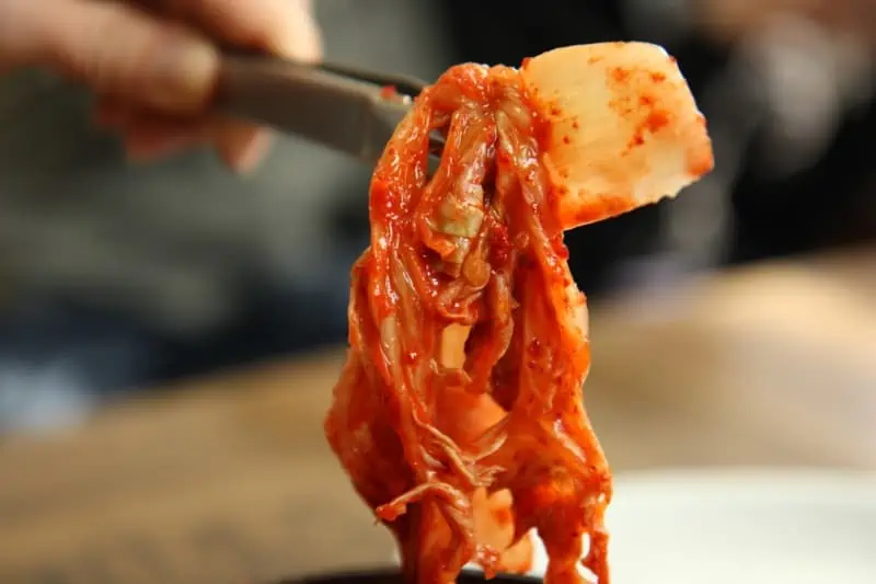 Some spicy, red coloured Korean Kimchi being held up with tongs