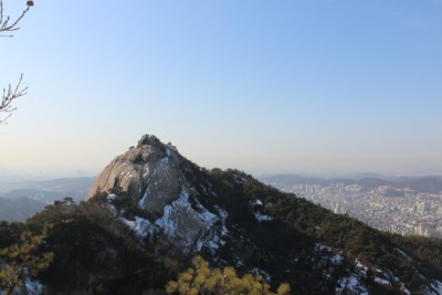 A view of Seoul can be seen from behind a jagged rock face in Bukhansan