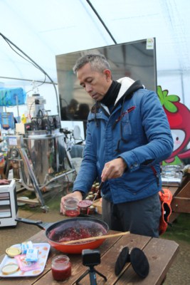 A man scooping strawberry jam into a jar with a ladle after making the jam in a frying pan.