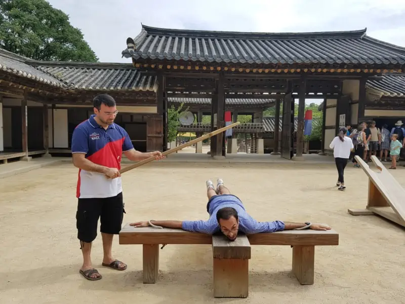 Two men experiencing what traditional punishment was like at the Korean Folk Village in Yongin