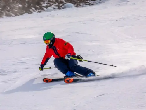 A man in red skiing quickly down a small beginner slope