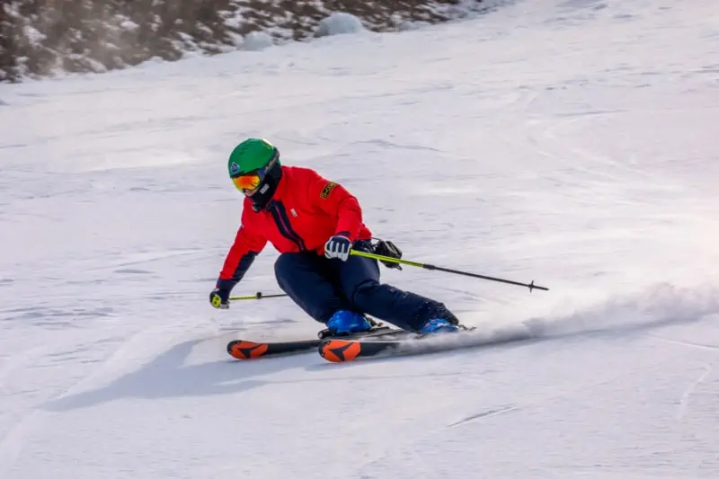 A man in red skiing quickly down a small beginner slope